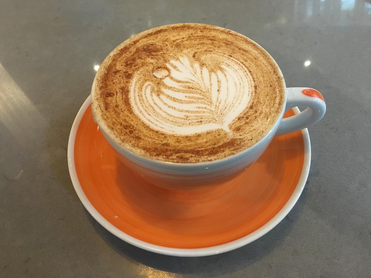 A latte with leaf art in an orange cup