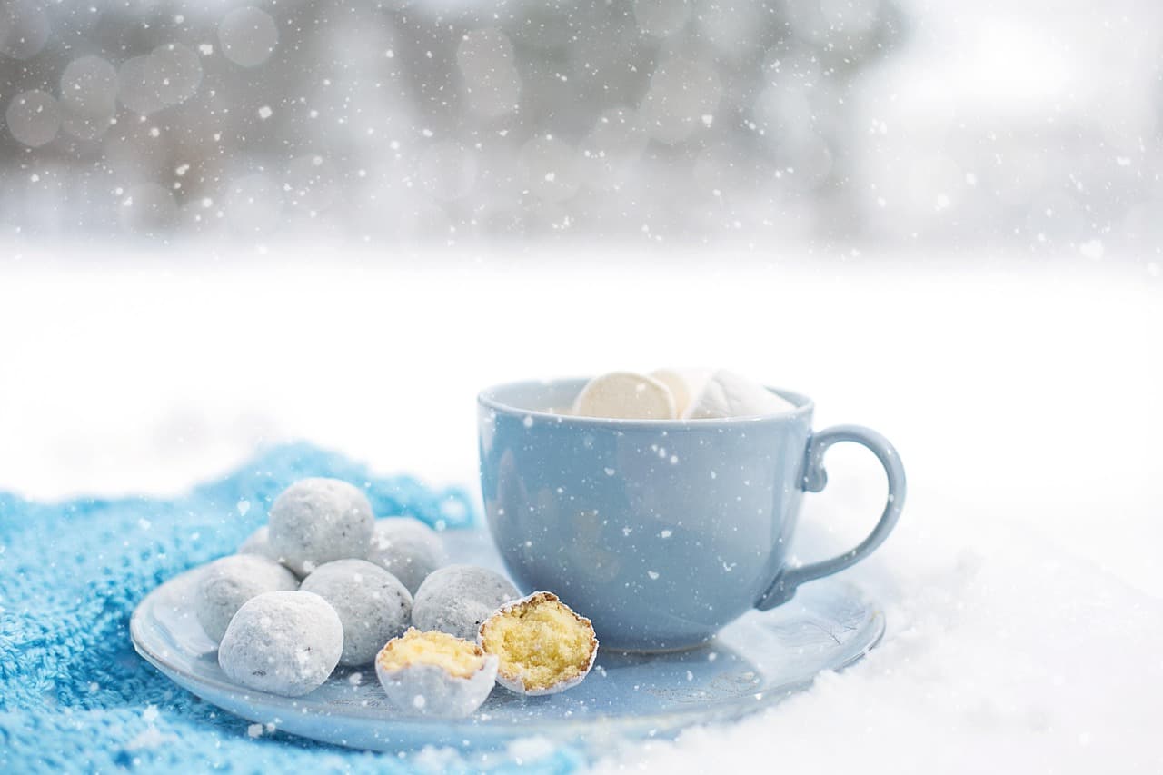 A hot chocolate in a blue mug with sweets on the saucer